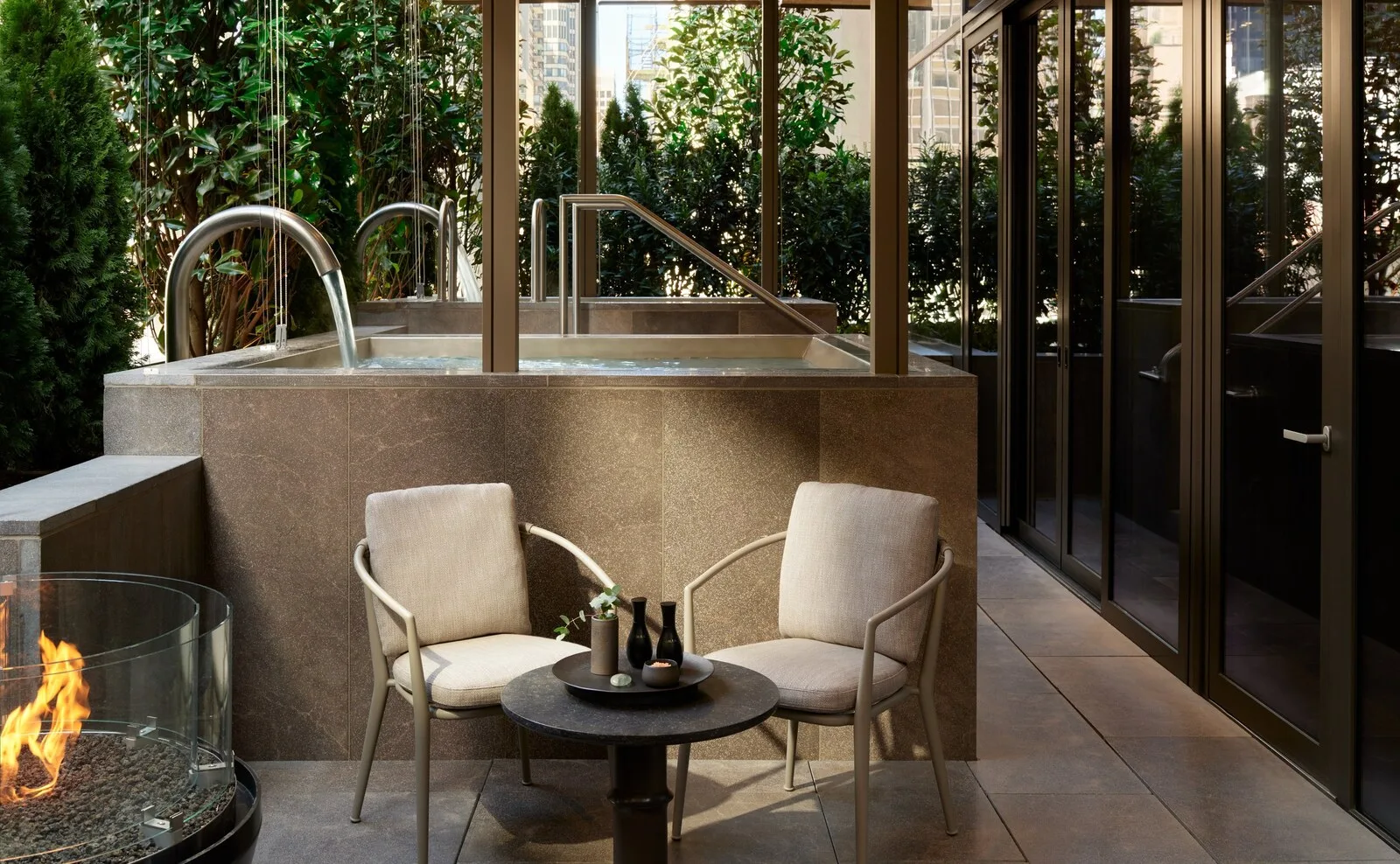 Water feature and lounge at Aman New York with greenery and a fire pit