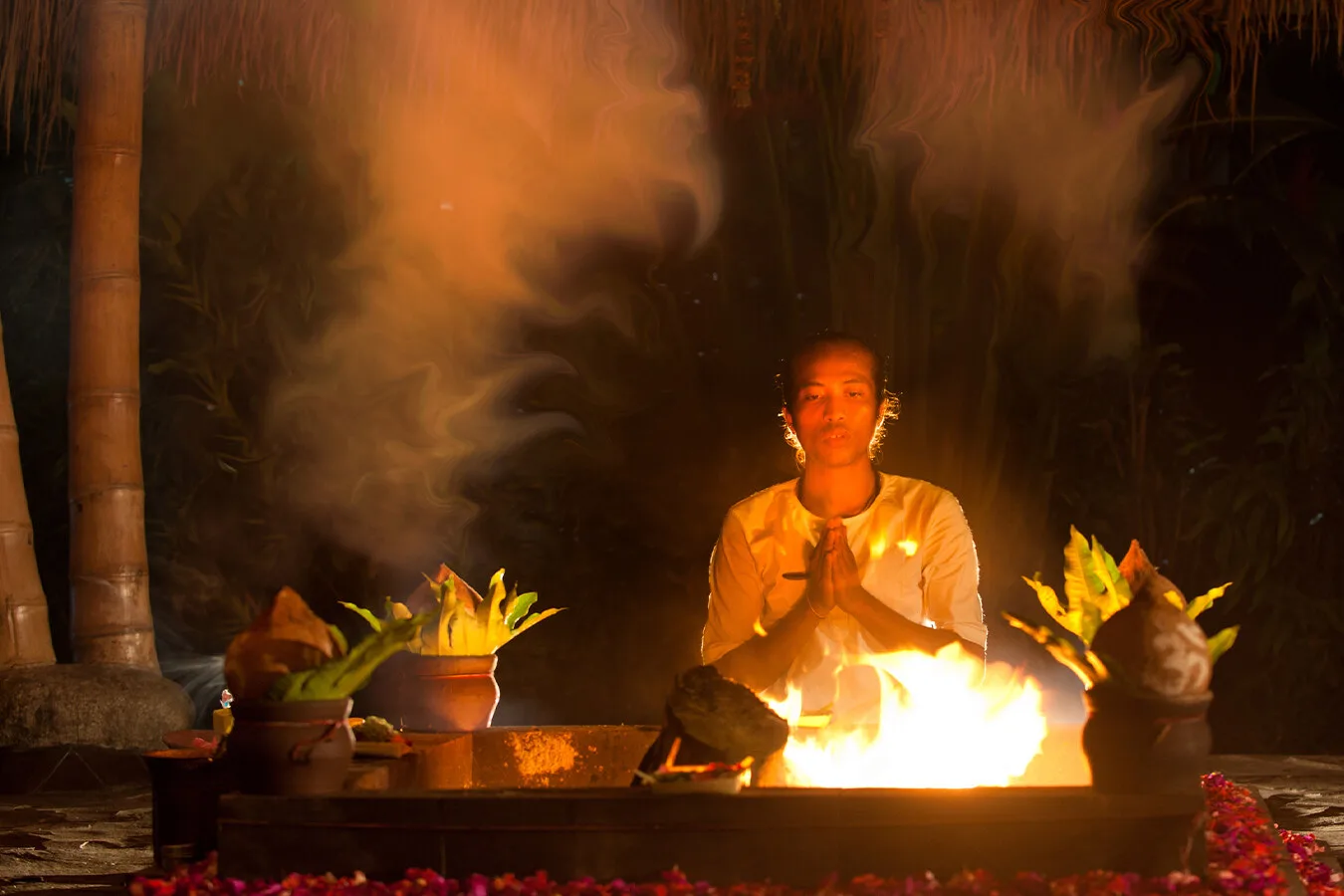 Person in white seated in prayer beside a fire ritual