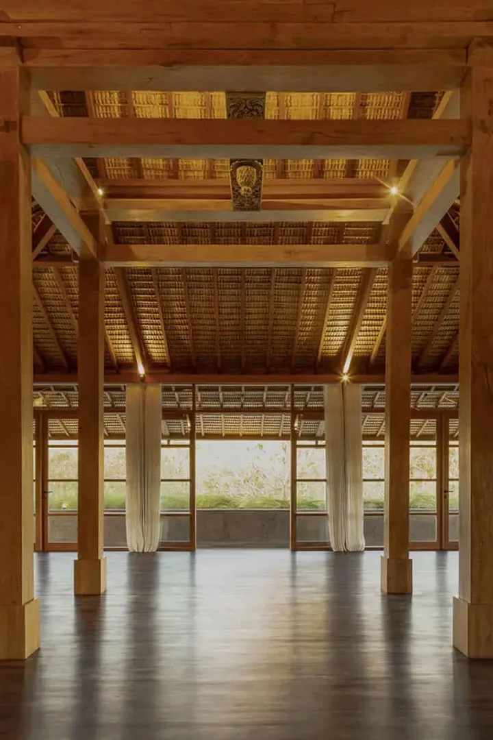 Open wooden yoga shala with polished floor and woven roof